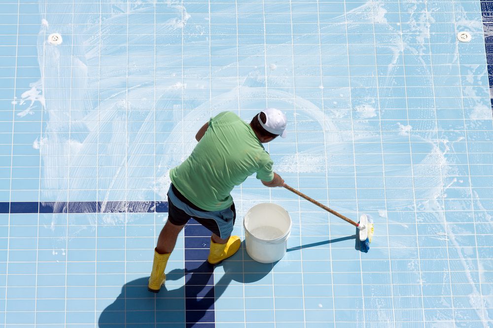 Operatore che spazzola il fondo di una piscina vuota
